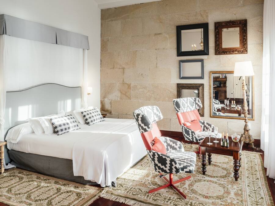 A hotel room with a bed, two armchairs, a small table, and a mirror.