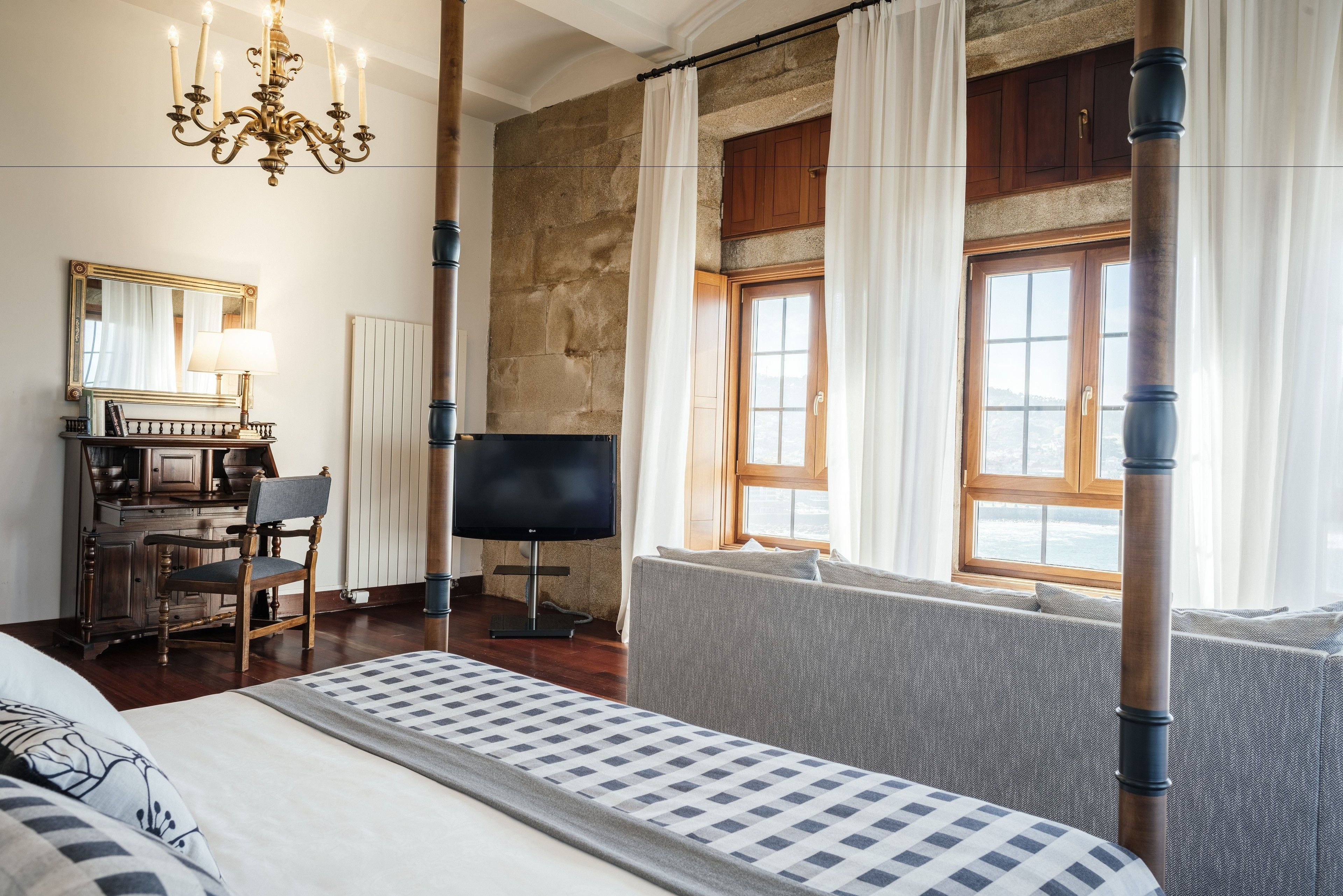 Habitación de hotel con una cama grande, televisión, escritorio con silla, espejo y ventana con cortinas.