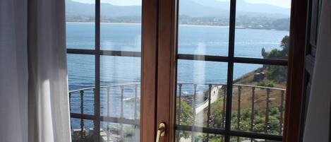 A view through a wooden-framed glass door to a balcony with a railing overlooking a body of water and distant mountains.