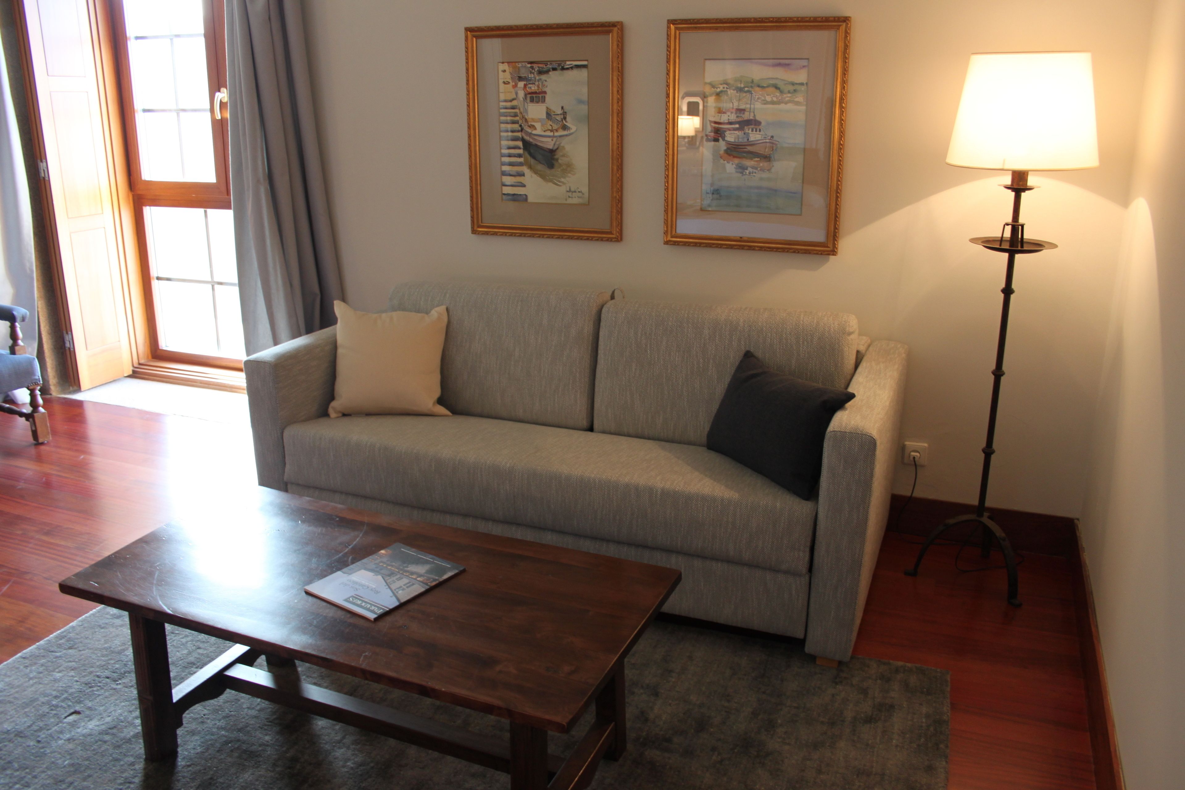 A living room with a sofa, a coffee table, a lamp, and two framed pictures on the wall.