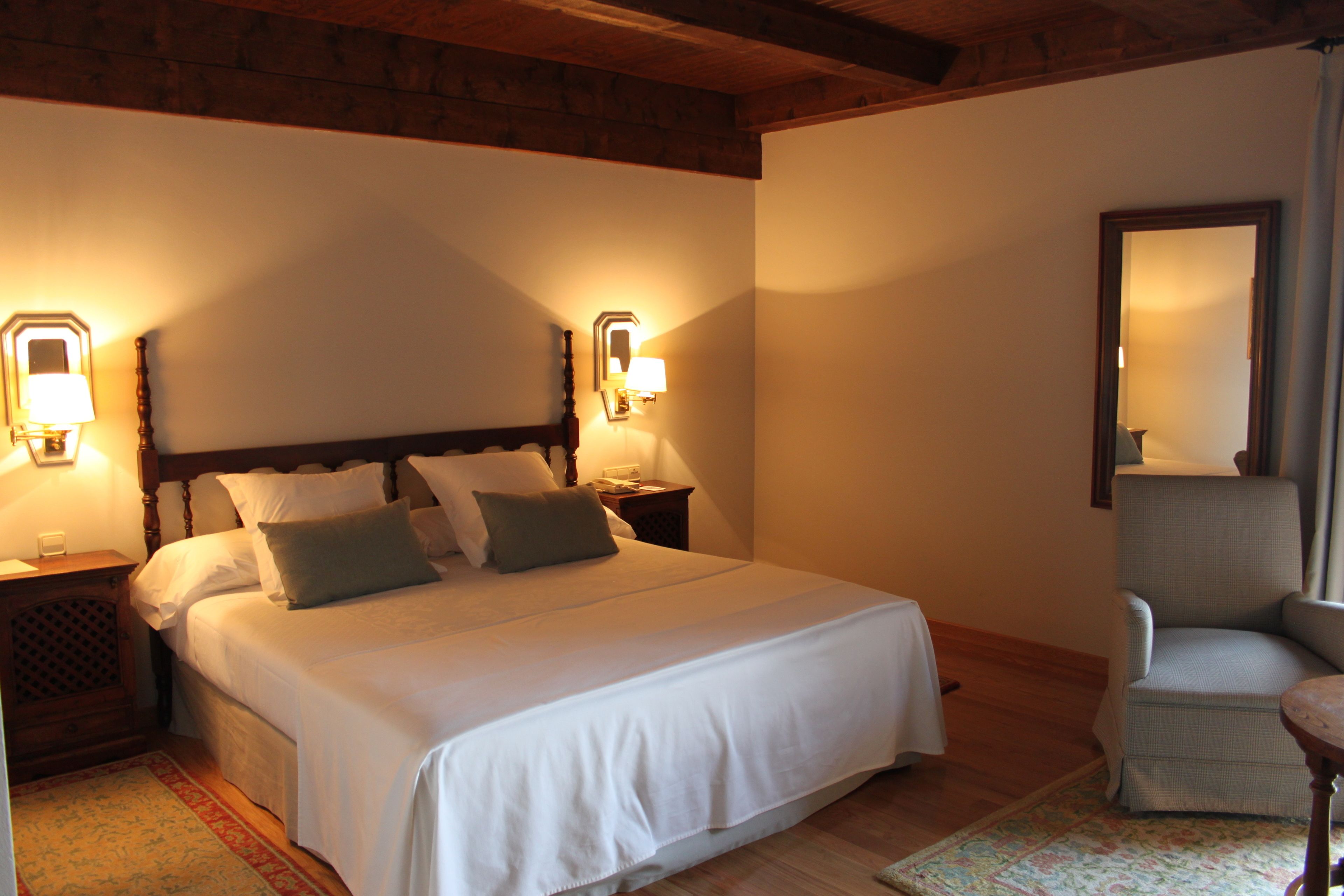 Un dormitorio con una cama grande, dos mesitas de noche con lámparas, una silla y un espejo en la pared.