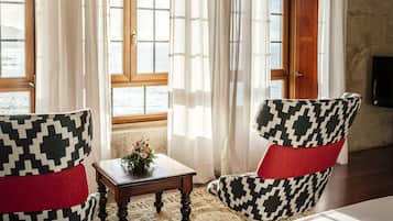 Una habitación con una cama, dos sillones estampados, una mesita con un florero y una ventana con cortinas.