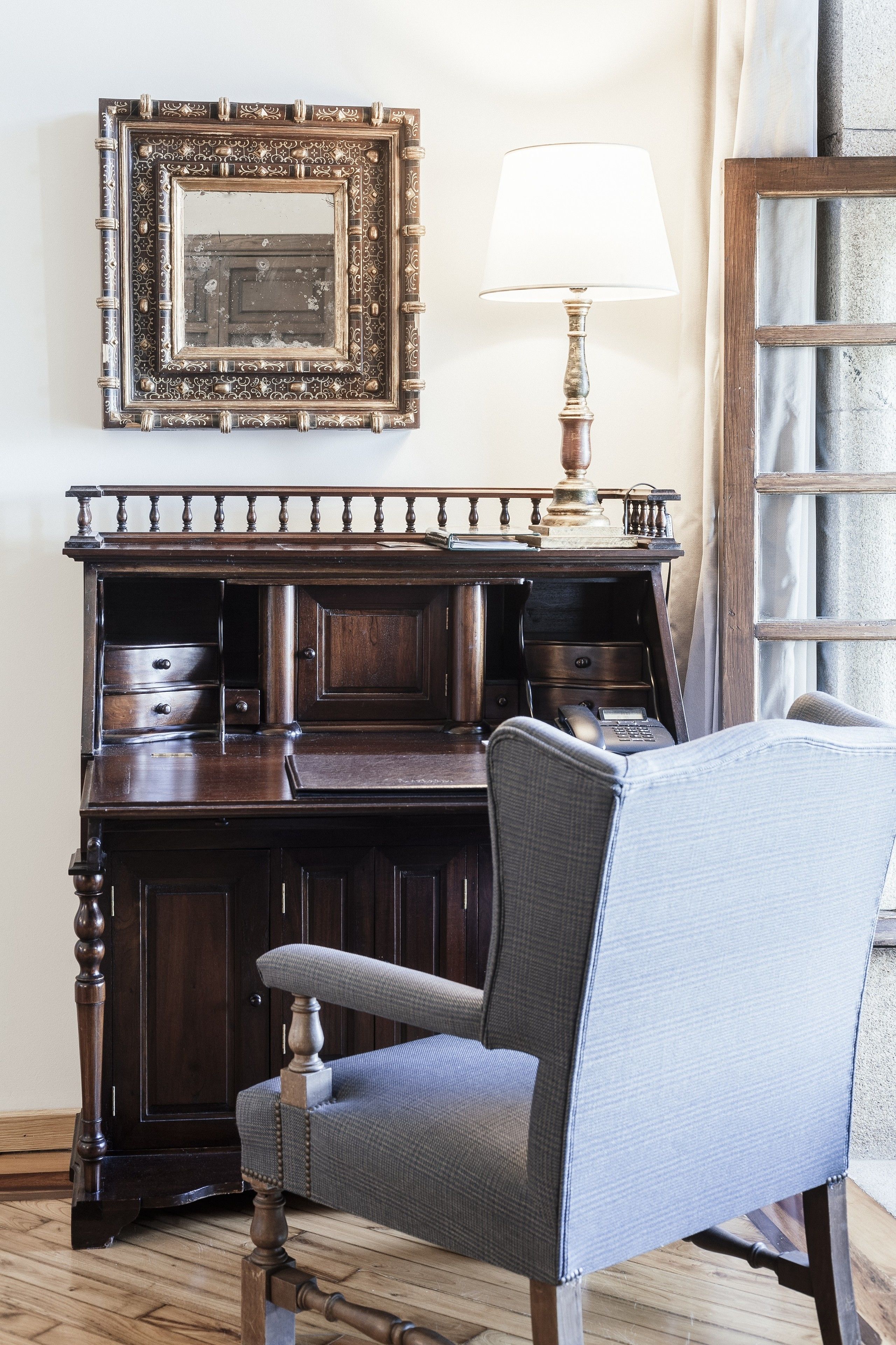 A wooden desk with drawers, a lamp, and a chair.