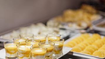 Un bufé con diversos postres, incluyendo una bandeja de cubos de crema pastelera amarilla y varios vasos de postre en capas.