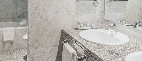 Un baño moderno con paredes de mármol, dos lavamanos, un espejo grande y cabina de ducha con paredes de vidrio.