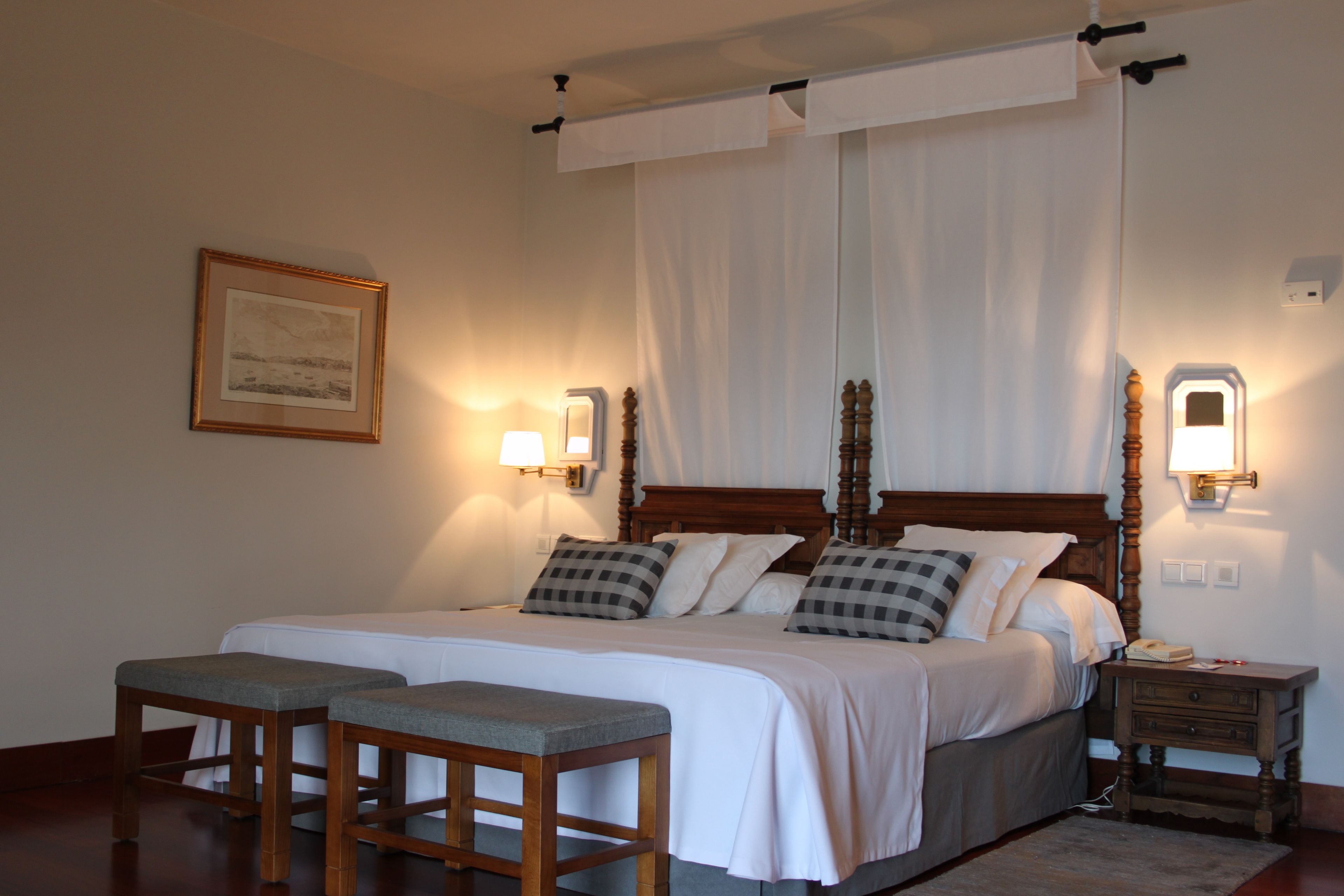 Ein ordentlich eingerichtetes Schlafzimmer mit einem großen Bett, zwei Nachttischen, einer Nachttischlampe und einem gerahmten Bild an der Wand.