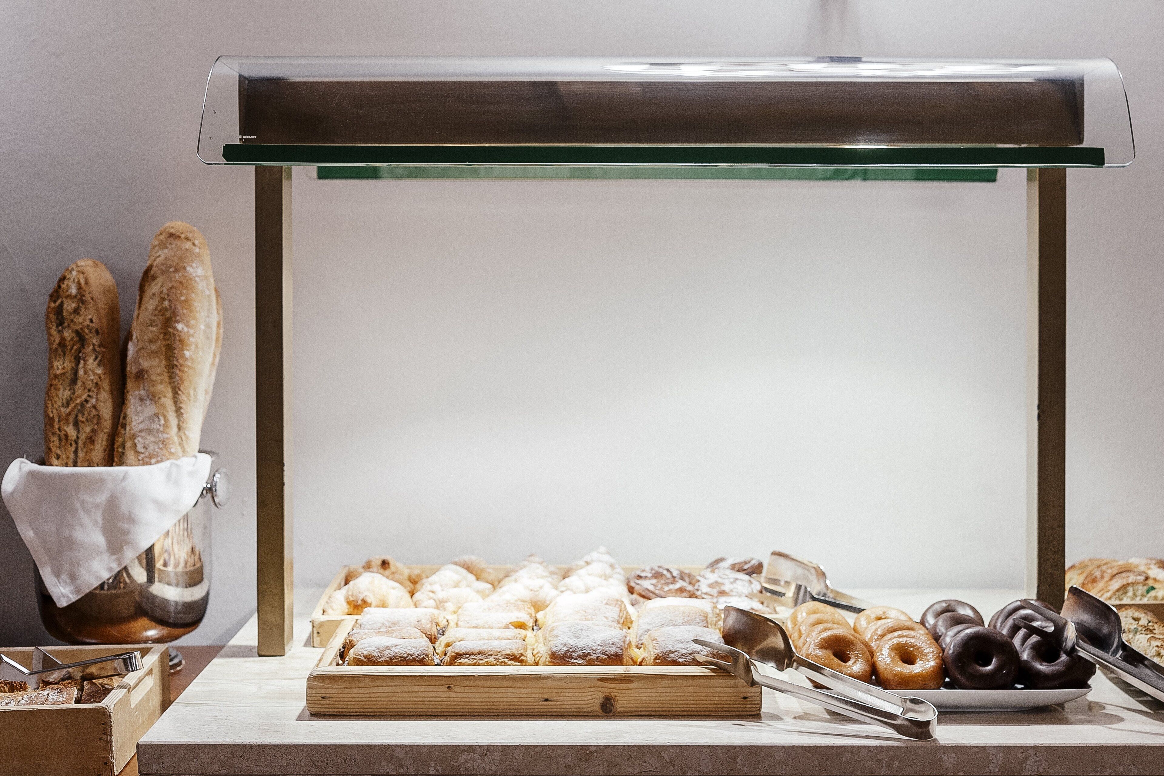 A bakery display with various pastries and bread, including donuts and a baguette, on a wooden board.