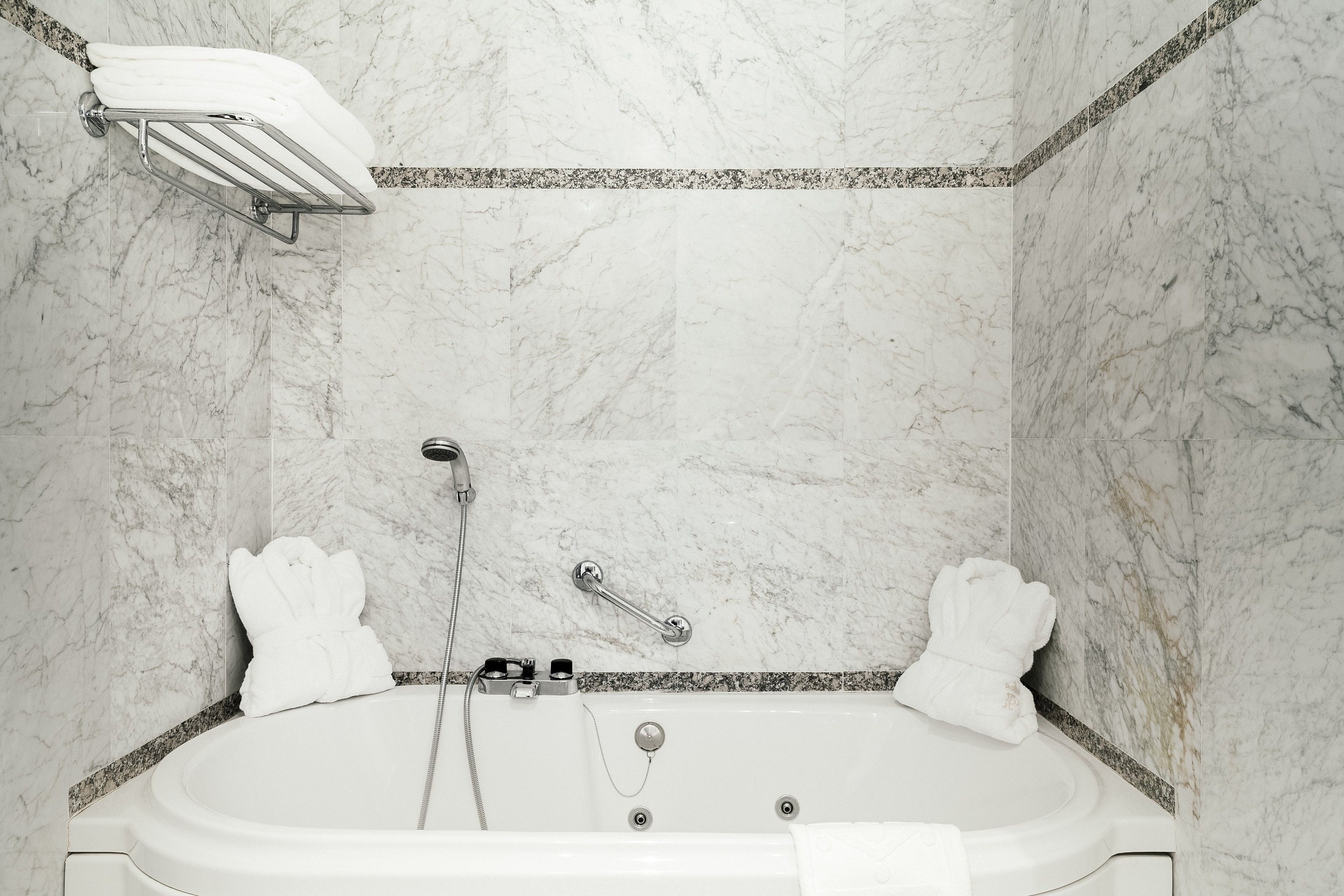 Un baño con pared de mármol, una bañera, una ducha y un perchero para toallas.
