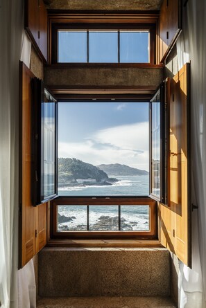 Quarto com uma ampla janela de sacada com vista para o oceano, com armários de madeira e piso coberto por carpete.