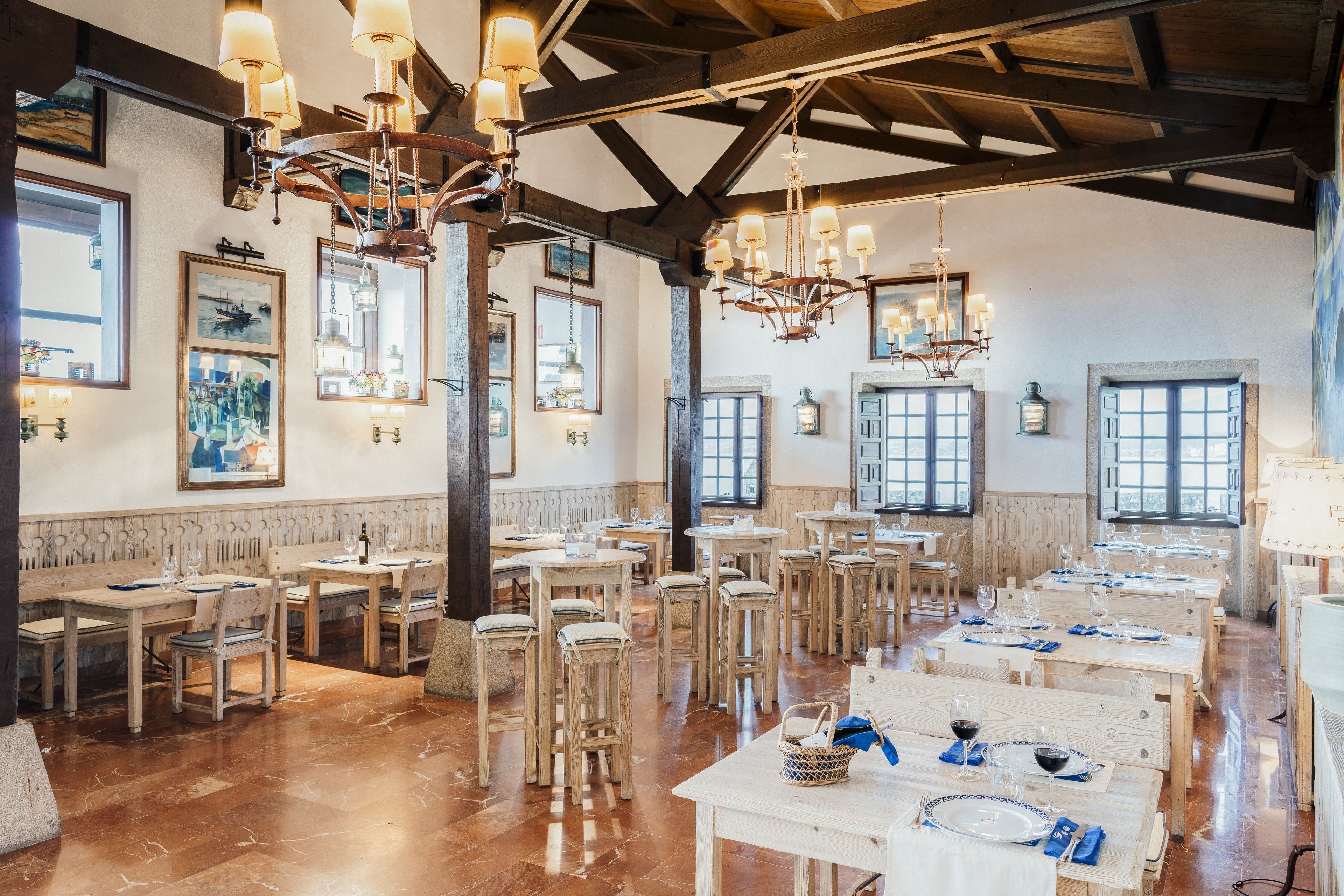 Une salle à manger spacieuse, avec des tables et des chaises en bois, des lustres et de grandes fenêtres.