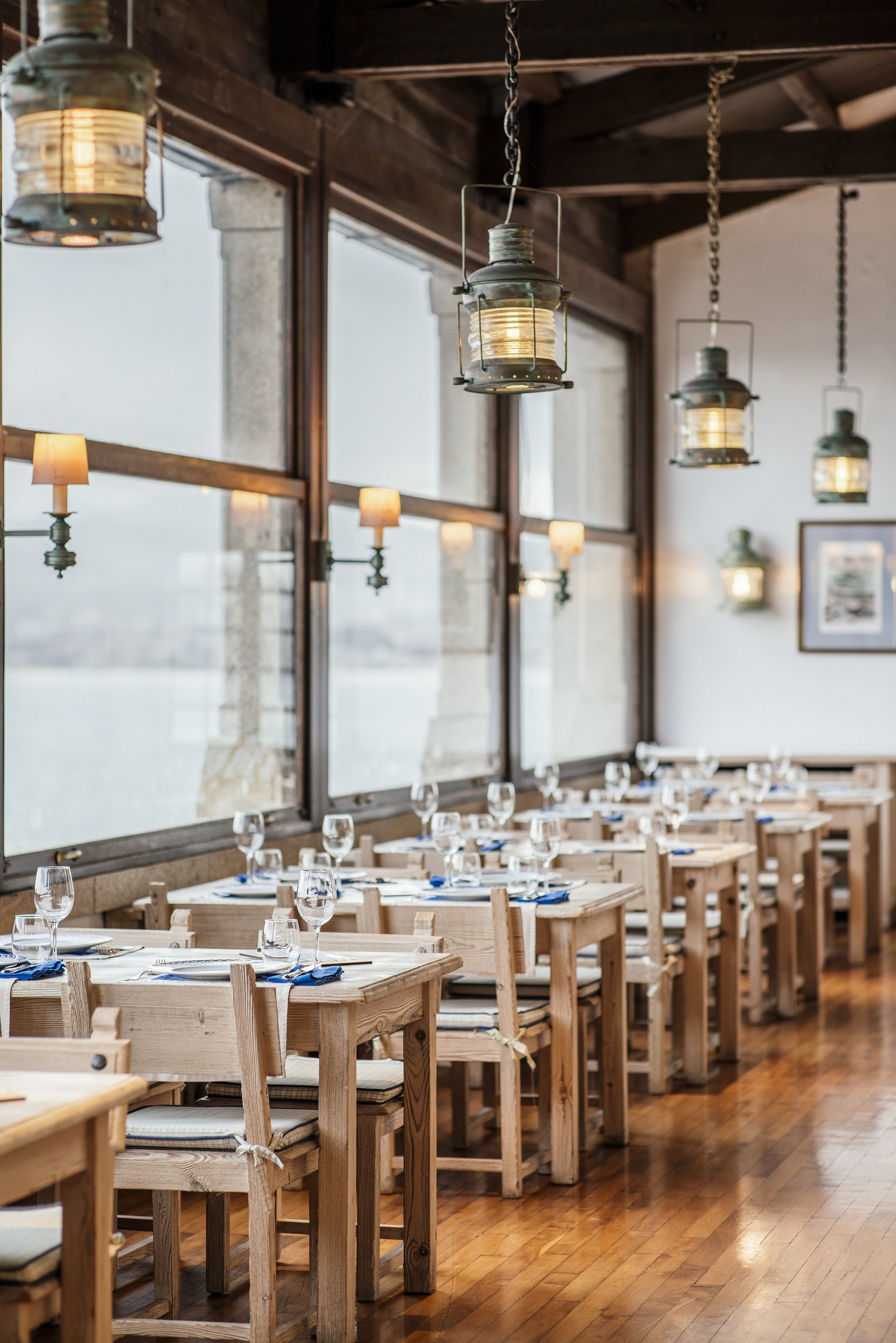 Un restaurant avec des tables et des chaises en bois, des lanternes suspendues et de grandes fenêtres.