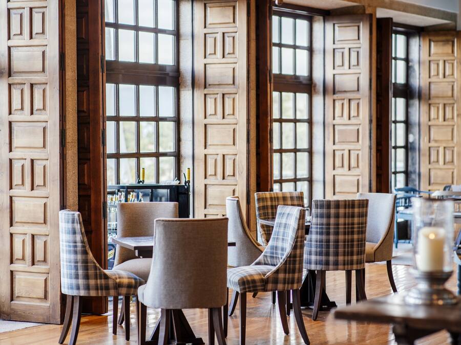 Un interior de restaurante con paredes de paneles de madera, sillas con estampado de cuadros y una vela sobre una mesa.