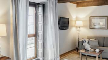 A hotel room with a bed, a desk with a laptop, a sofa, a TV, and a window with curtains.