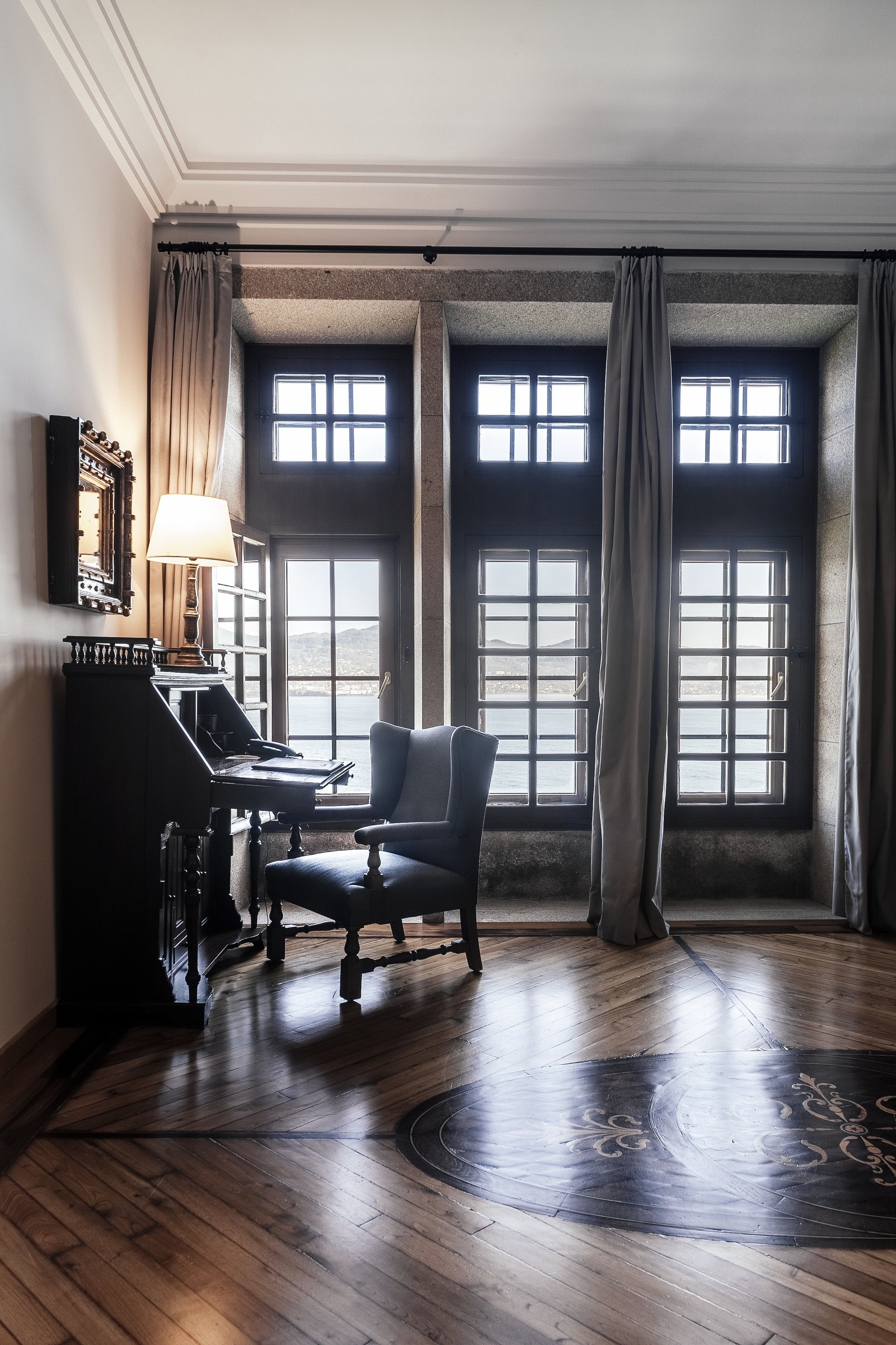 Una habitación con un piano, una silla y ventanas amplias con cortinas.