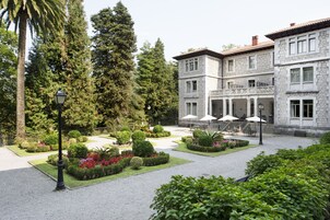 Un patio con un edificio de piedra, rodeado de jardines y árboles bien cuidados.