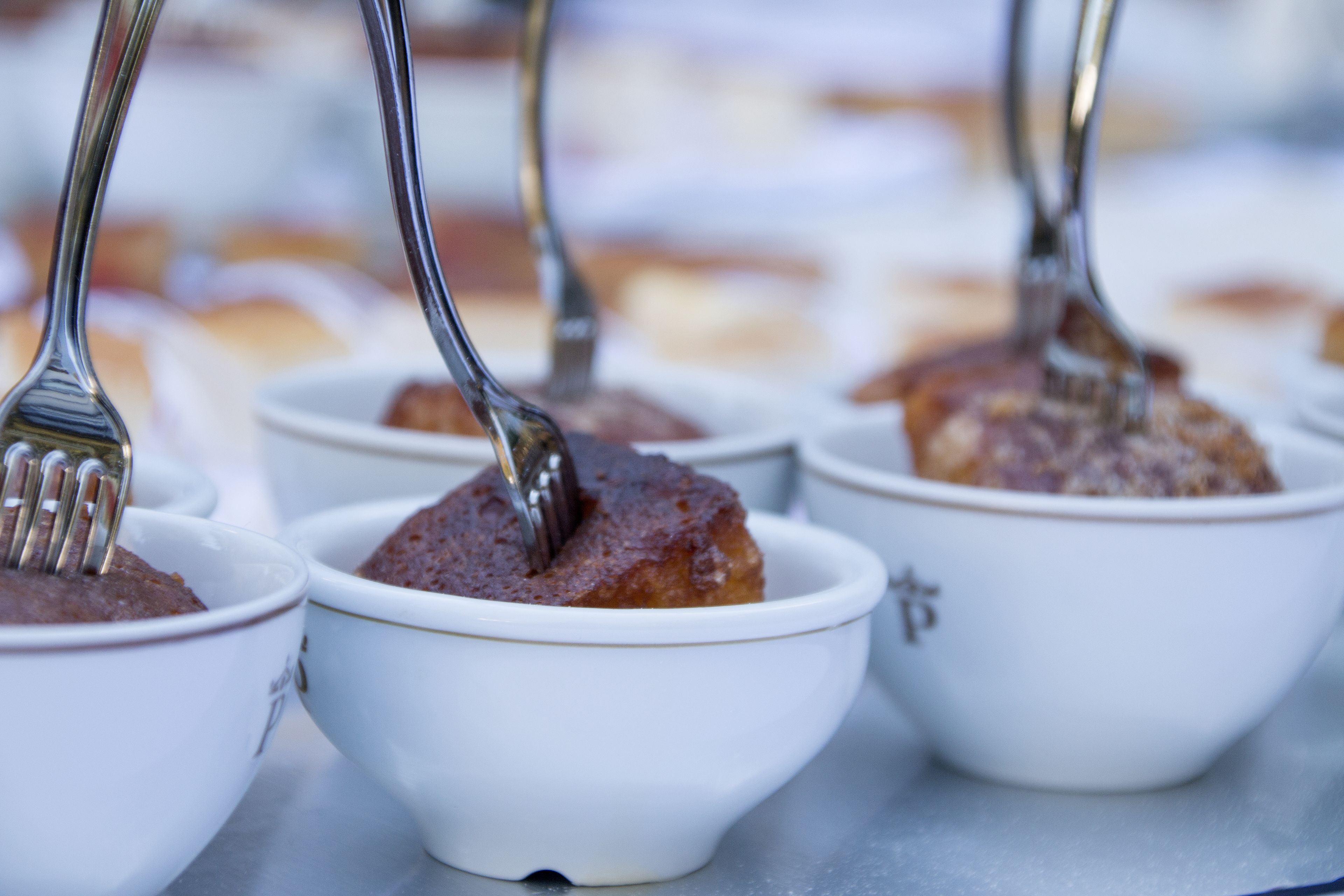 Una hilera de recipientes blancos con cucharas, que contienen un postre.
