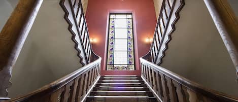 Una imponente escalera con barandillas ornamentadas y un ventanal de vidrio emplomado en la parte superior.