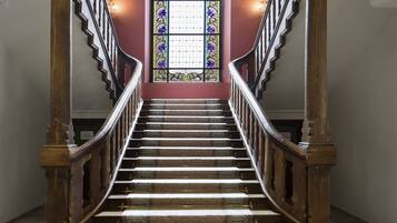 Una gran escalera con barandillas de madera ornamentadas y un suelo estampado que conduce a un vitral.