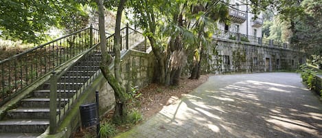 A stone staircase leading up to a building with a balcony, surrounded by lush greenery.