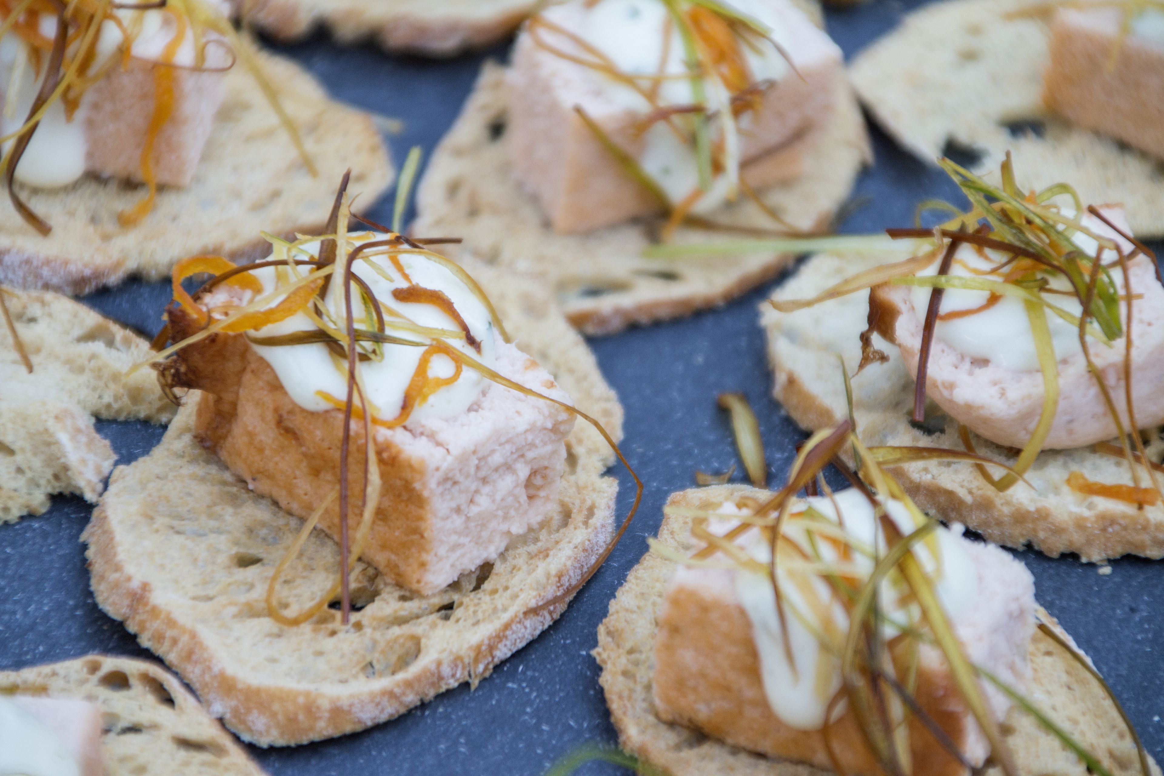 Primer plano de alimentos, probablemente aperitivos, sobre rebanadas de pan con fondo azul.