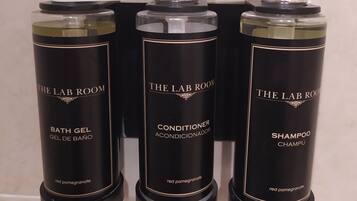 Three black bottles of The Lab Room products: bath gel, conditioner, and shampoo, with a pump dispenser on top.