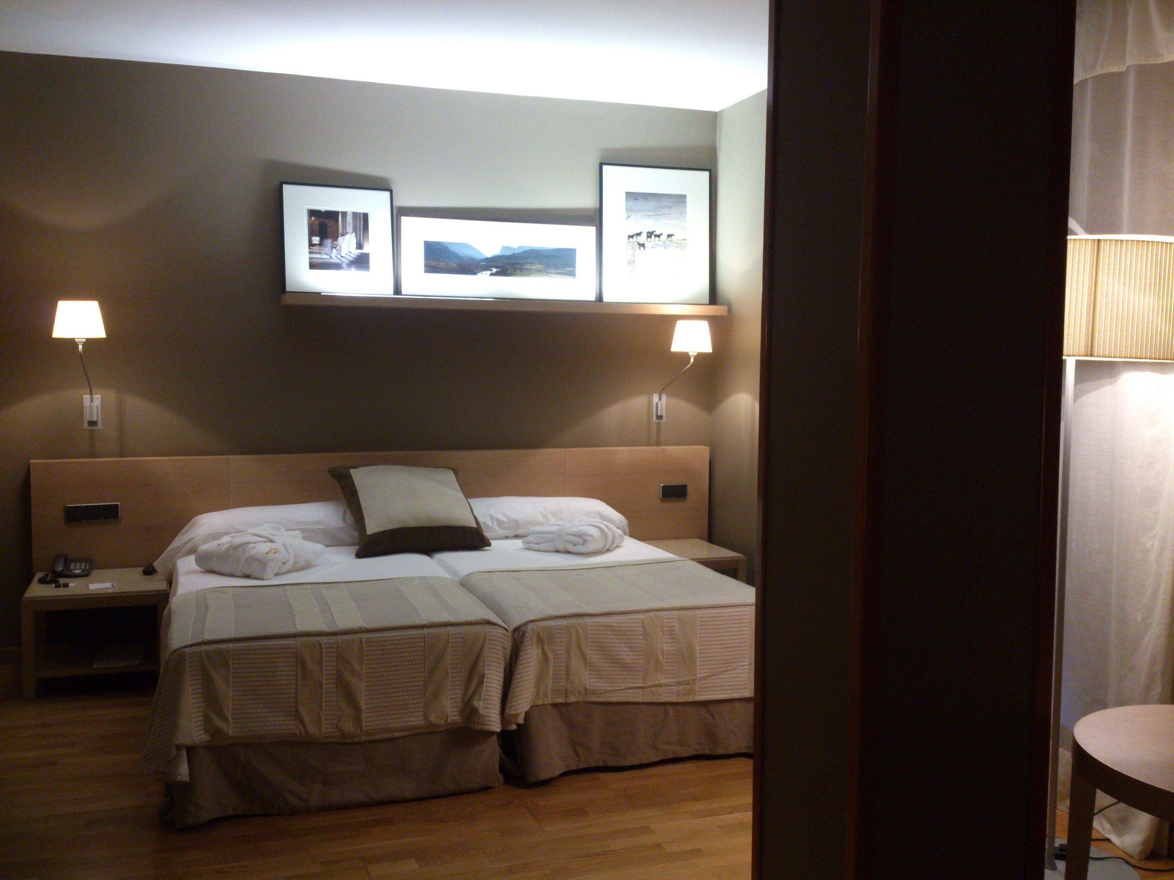 A hotel room with a double bed, two bedside tables, a nightstand, and wall-mounted lamps.