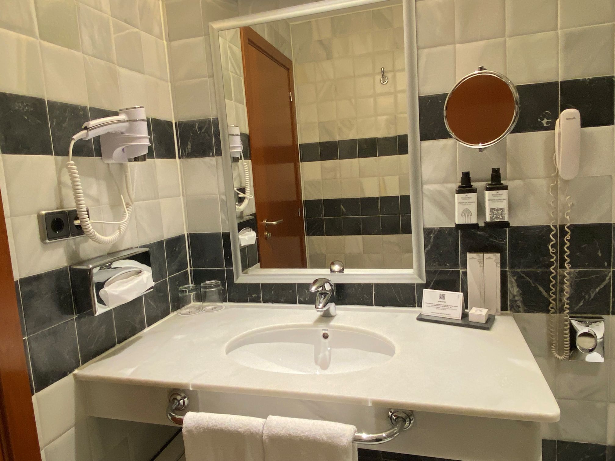 A bathroom with a white sink, a mirror, a hairdryer, and toiletries on the wall.