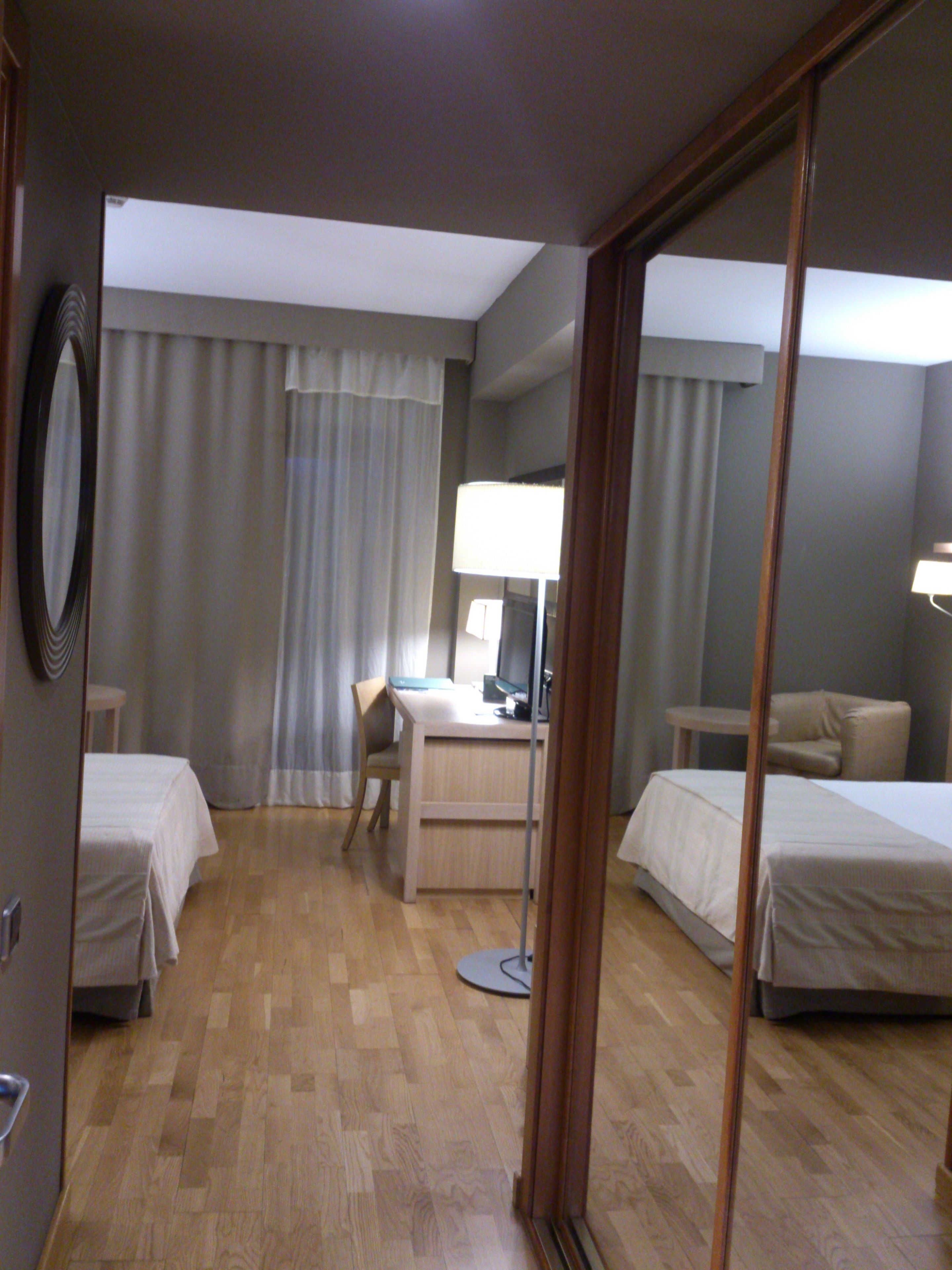A hotel room with two beds, a desk with a computer, a chair, and a lamp.