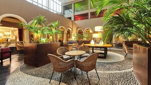 A spacious lobby with high ceilings, a central seating area with wicker chairs and a round table, and multiple potted plants. - Parador de la Seu d'Urgell (La Seu d'Urgell)