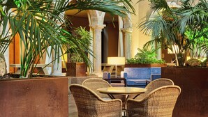 An indoor patio area with wicker furniture, potted plants, and a stone column structure. - Parador de la Seu d'Urgell (La Seu d'Urgell)