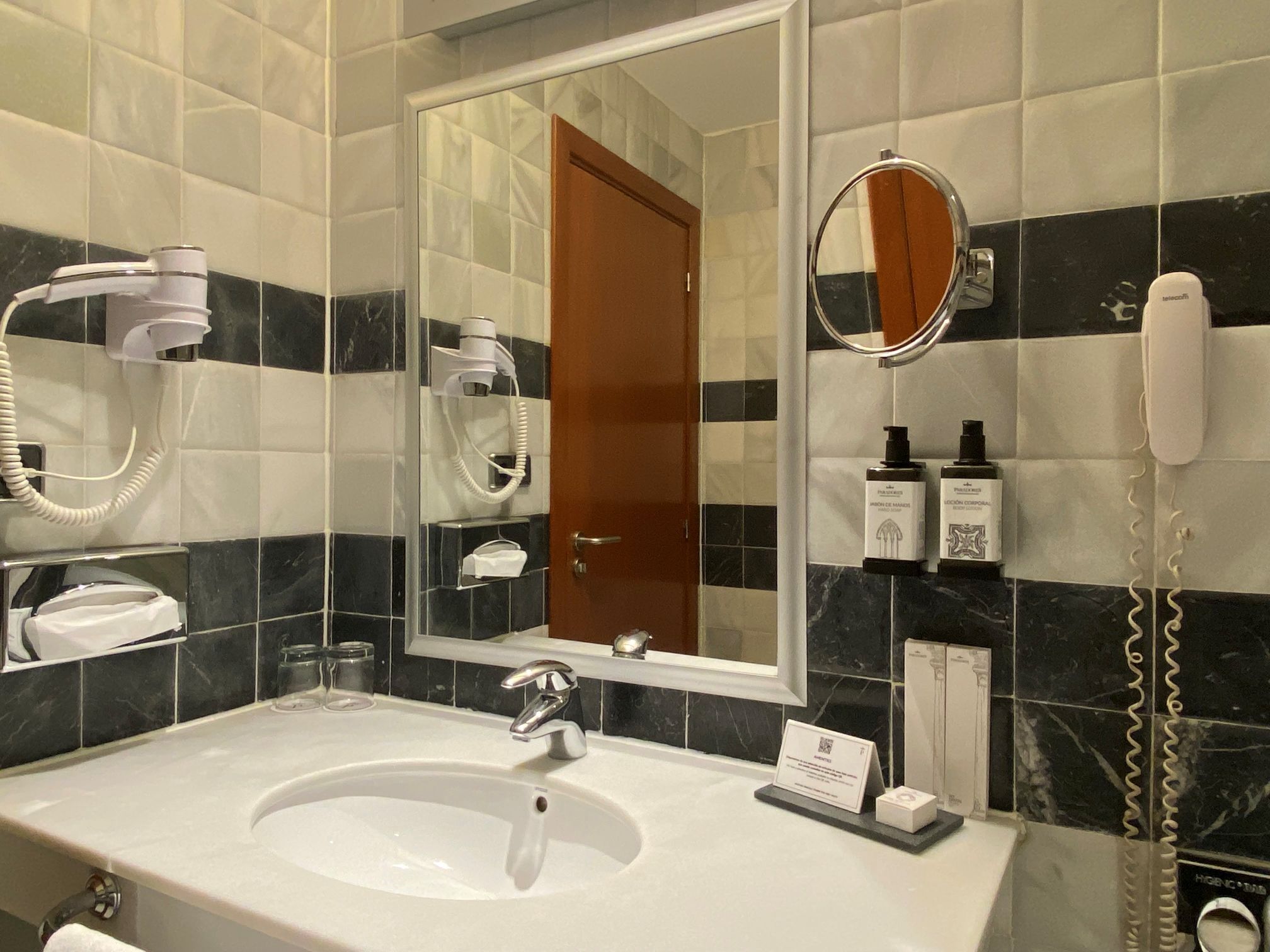 A hotel bathroom with a sink, mirror, hairdryer, and toiletries.