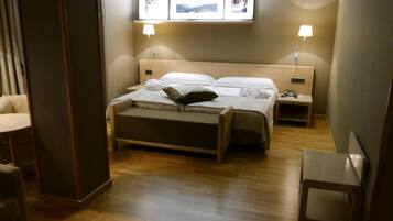 A hotel room with a bed, bedside tables, a desk, and a chair. There are framed pictures on the wall above the bed.