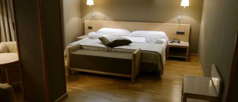 A hotel room with a bed, bedside tables, a desk, and a chair. There are framed pictures on the wall above the bed.