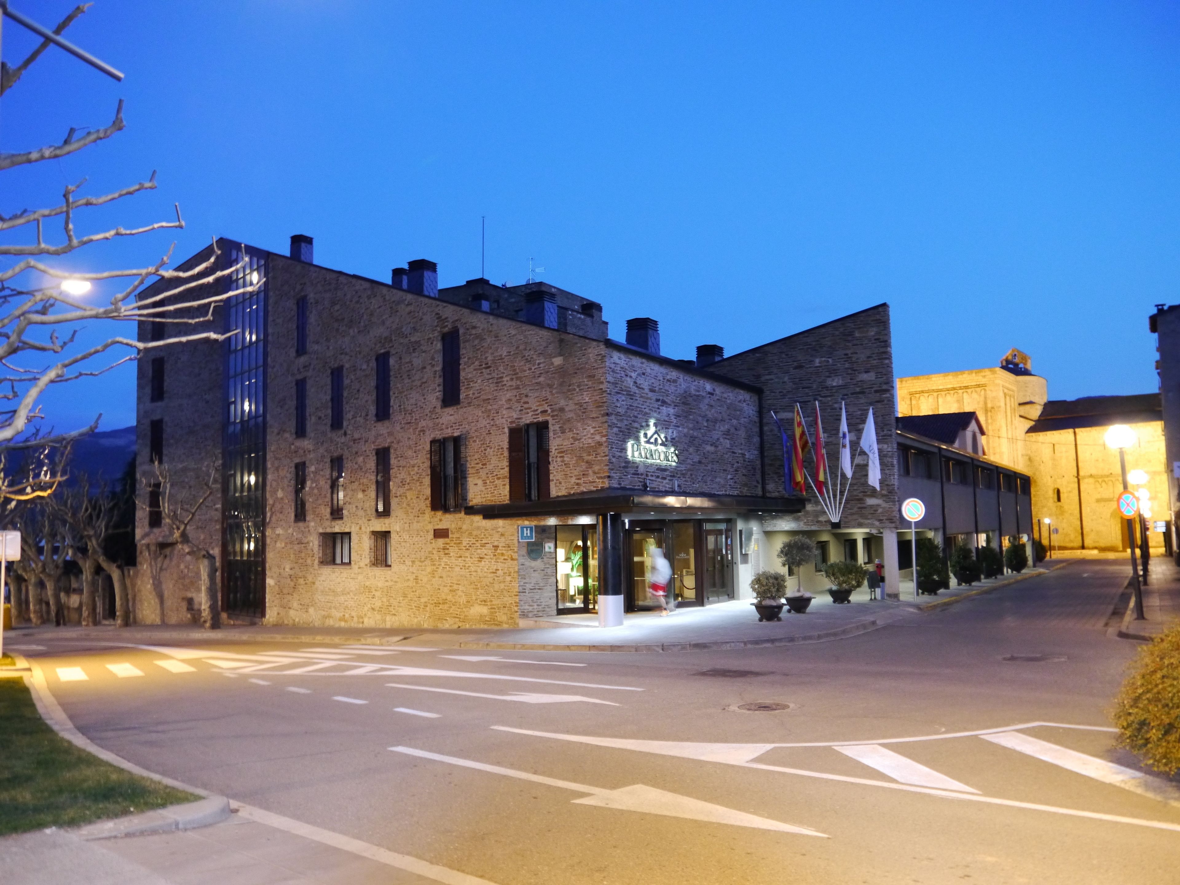 A hotel with a stone facade, a visible entrance, and flags outside.