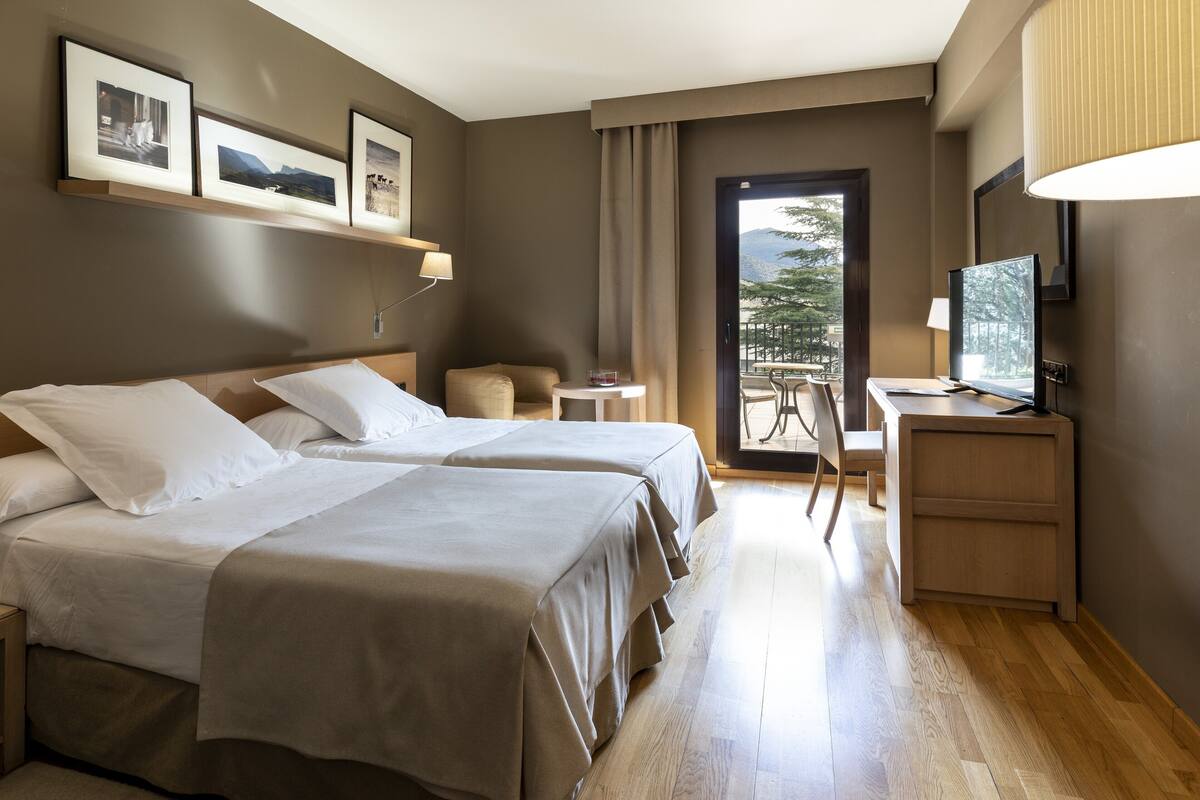 A hotel room with two beds, a desk, a chair, and a TV.