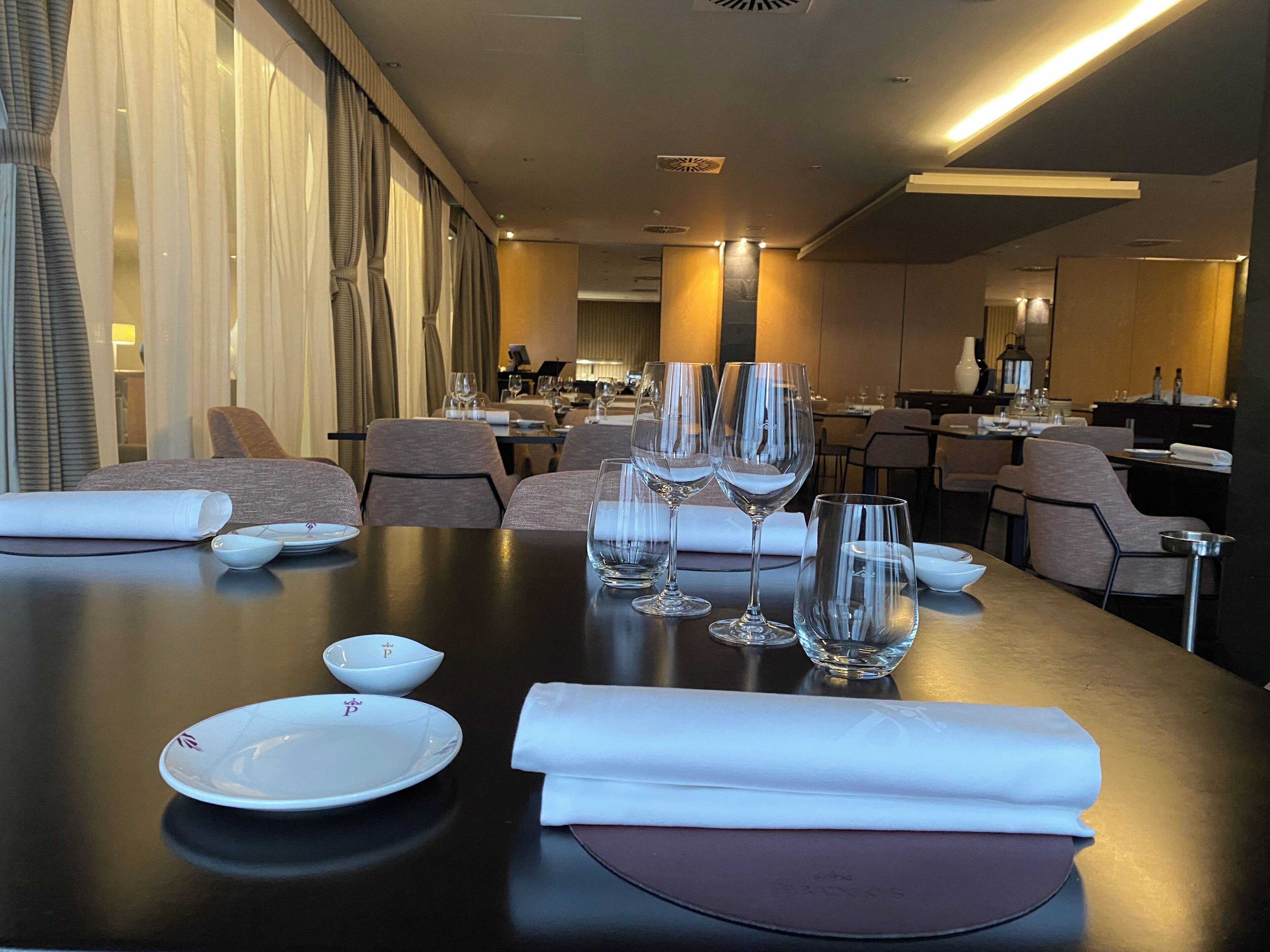 Une table à manger dressée avec des assiettes blanches, des bols et des verres à vin, et une serviette pliée posée sur la table.
