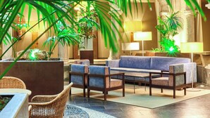 A lobby with a blue sofa, wicker chairs, a coffee table, and potted plants. - Parador de la Seu d'Urgell (La Seu d'Urgell)
