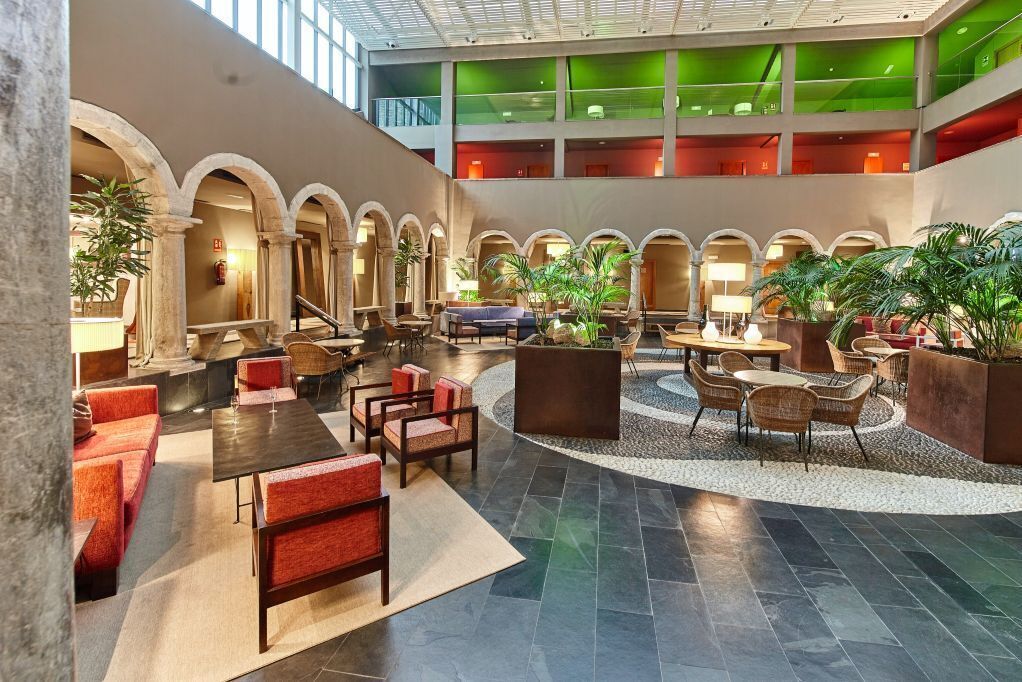 Un hall d’entrée spacieux doté d’un espace salon central, de nombreuses arcades et d’un plafond haut avec des vitres teintées de vert.