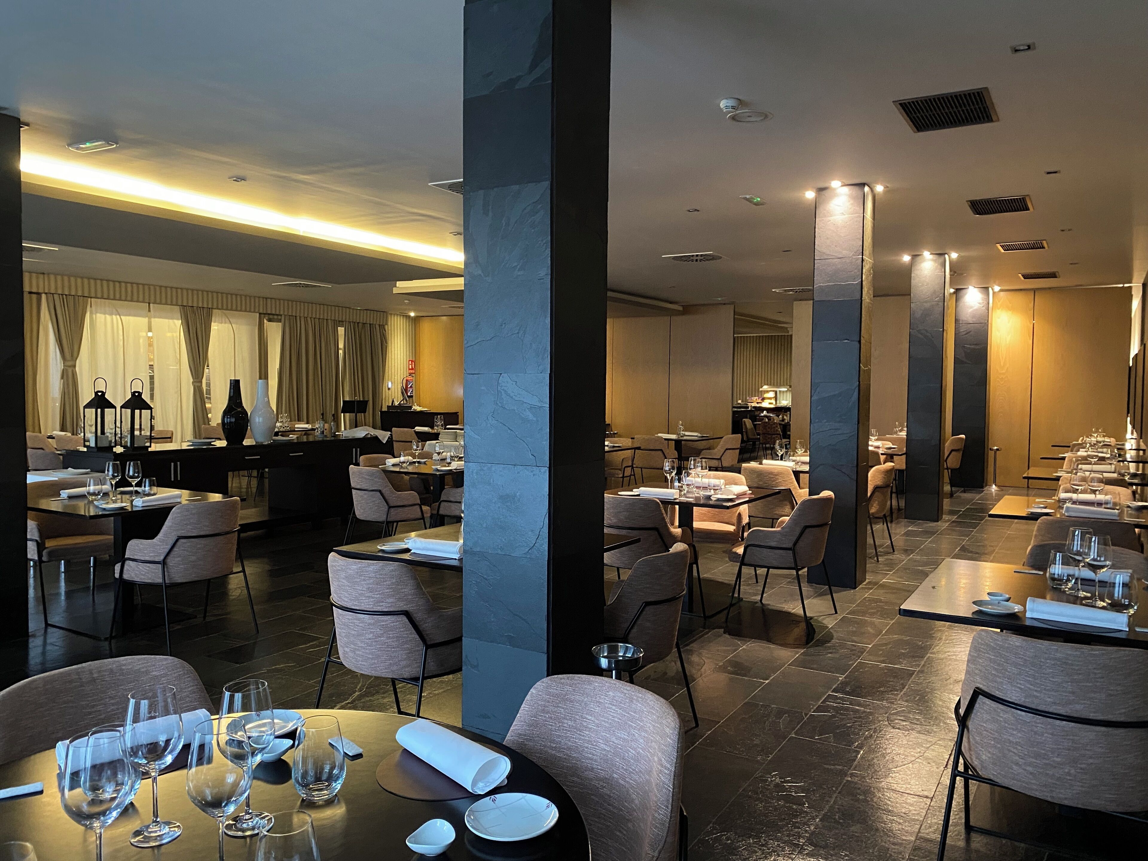 Un restaurante moderno con techos altos, iluminación ambiental y un interior limpio y minimalista.