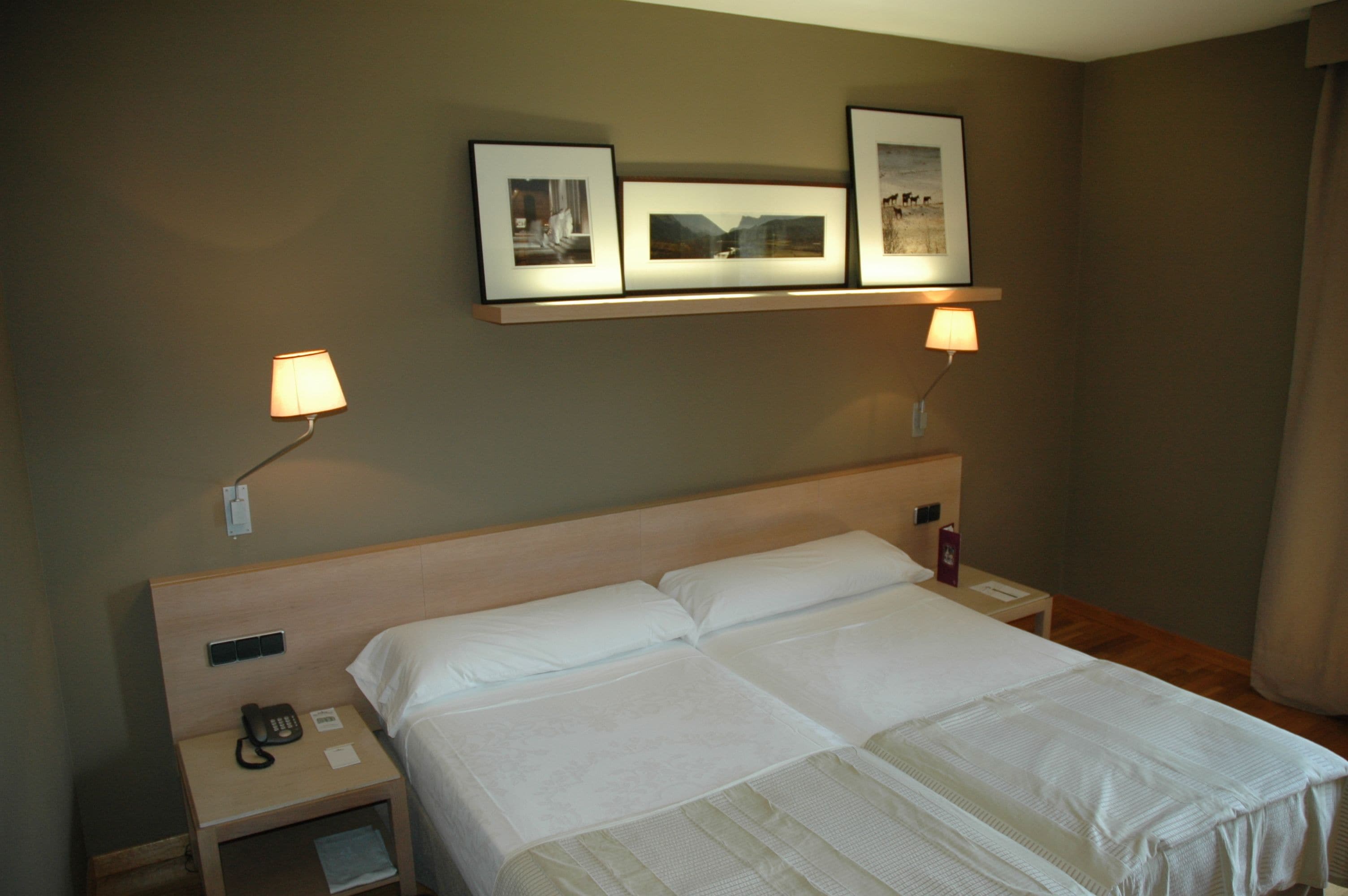 A hotel room with a large bed, bedside lamps, a phone on the nightstand, and framed pictures on the wall.