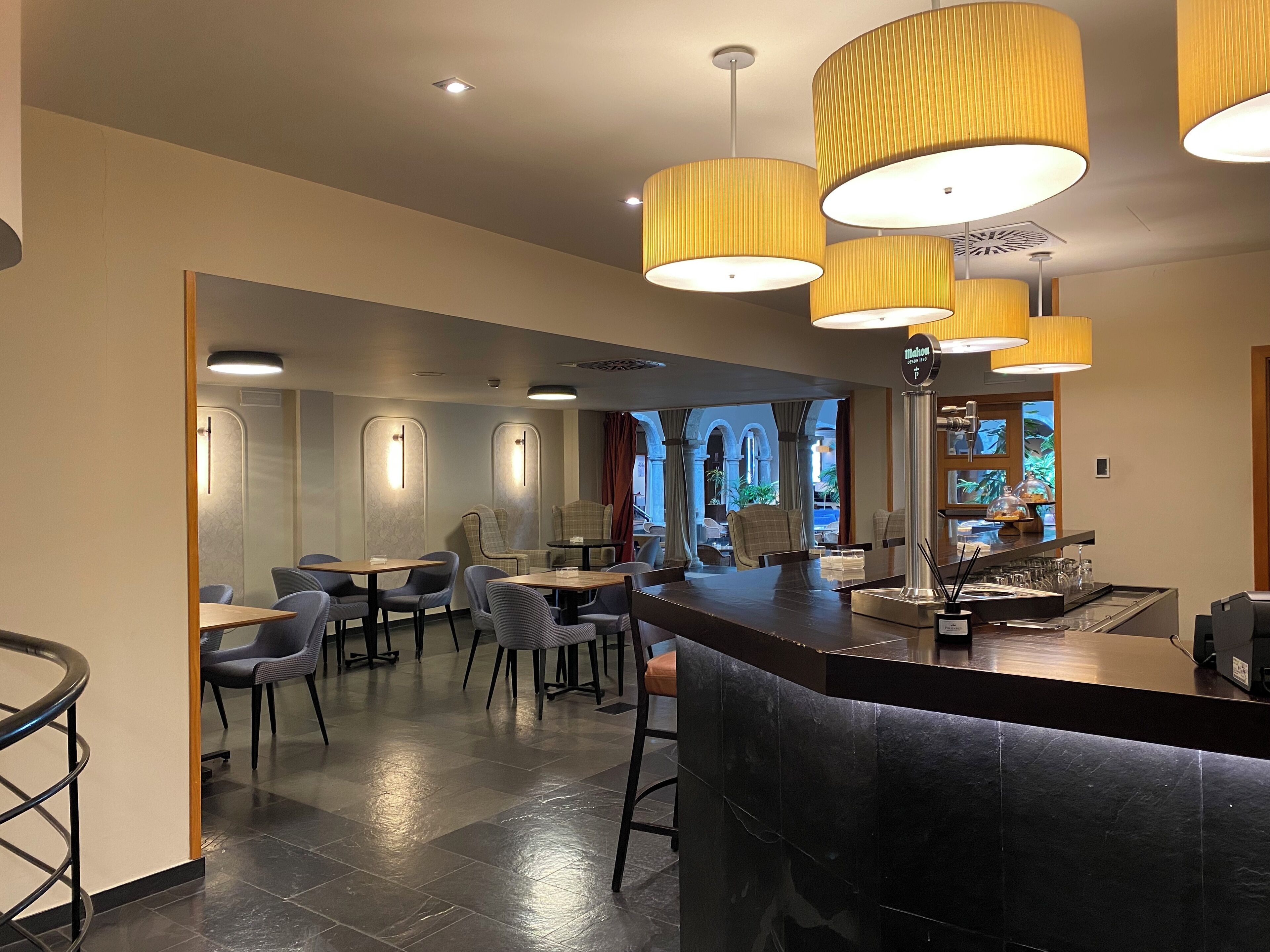 A modern hotel lobby with a bar area, seating arrangements, and a view of the outdoors.