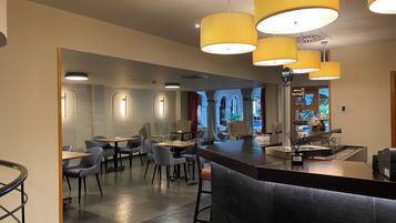 A modern hotel lobby with a bar area, seating arrangements, and a view of the outdoors.
