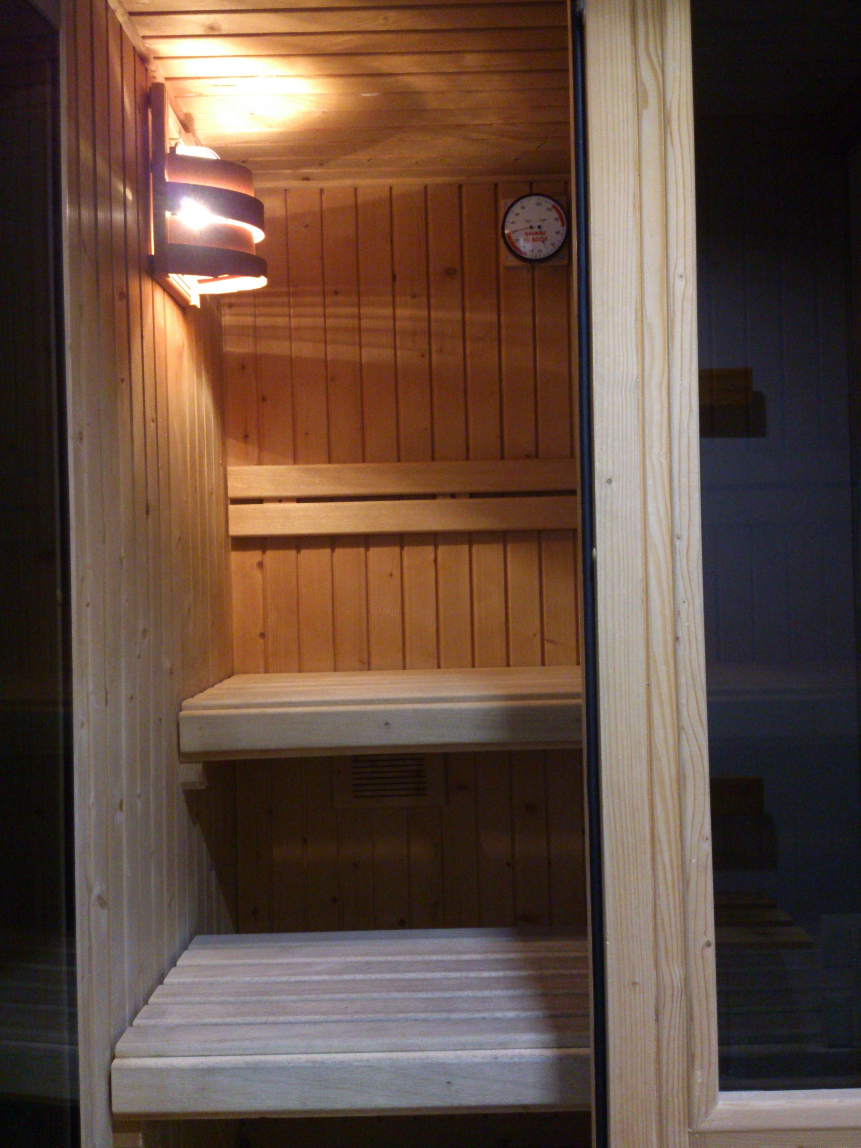 A wooden sauna with a bench and a wall-mounted thermometer.