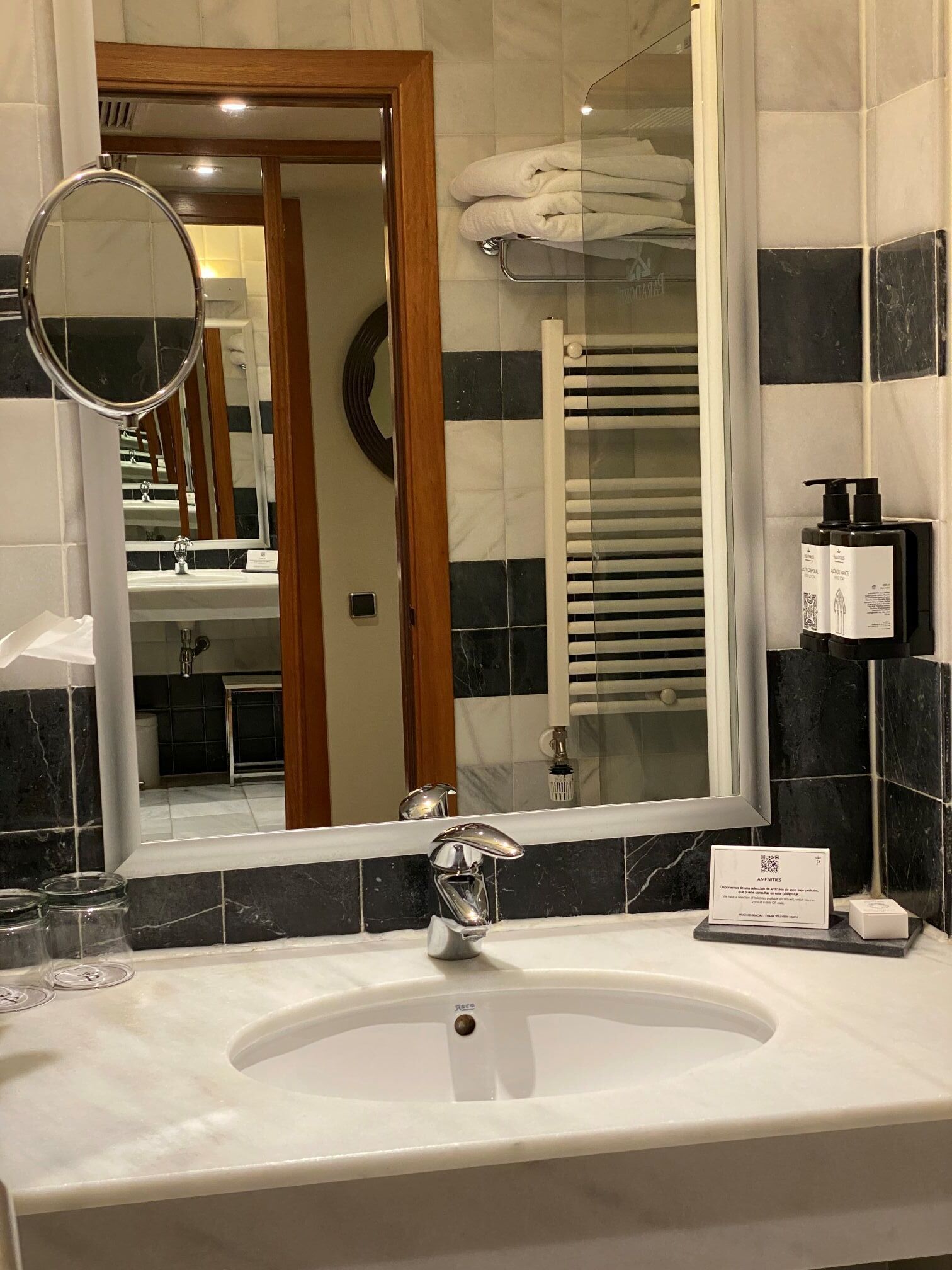 Une salle de bain d’hôtel avec un grand miroir, un lavabo et un porte-serviettes.