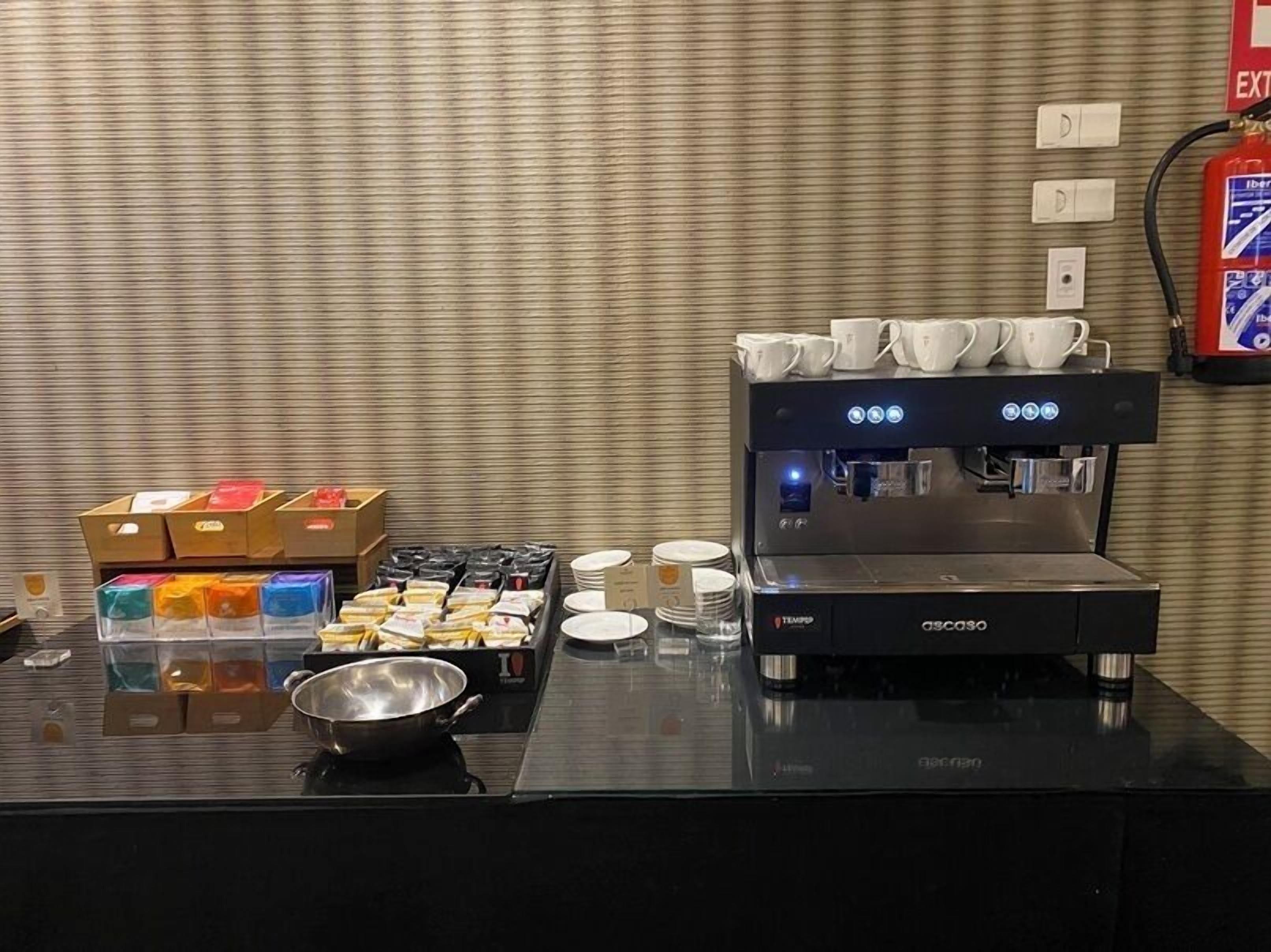 Una estación de café con una máquina de espresso, tazas y diferentes opciones de comida.