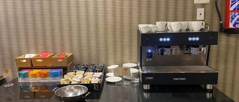 Una estación de café con una máquina de espresso, tazas y diferentes opciones de comida.