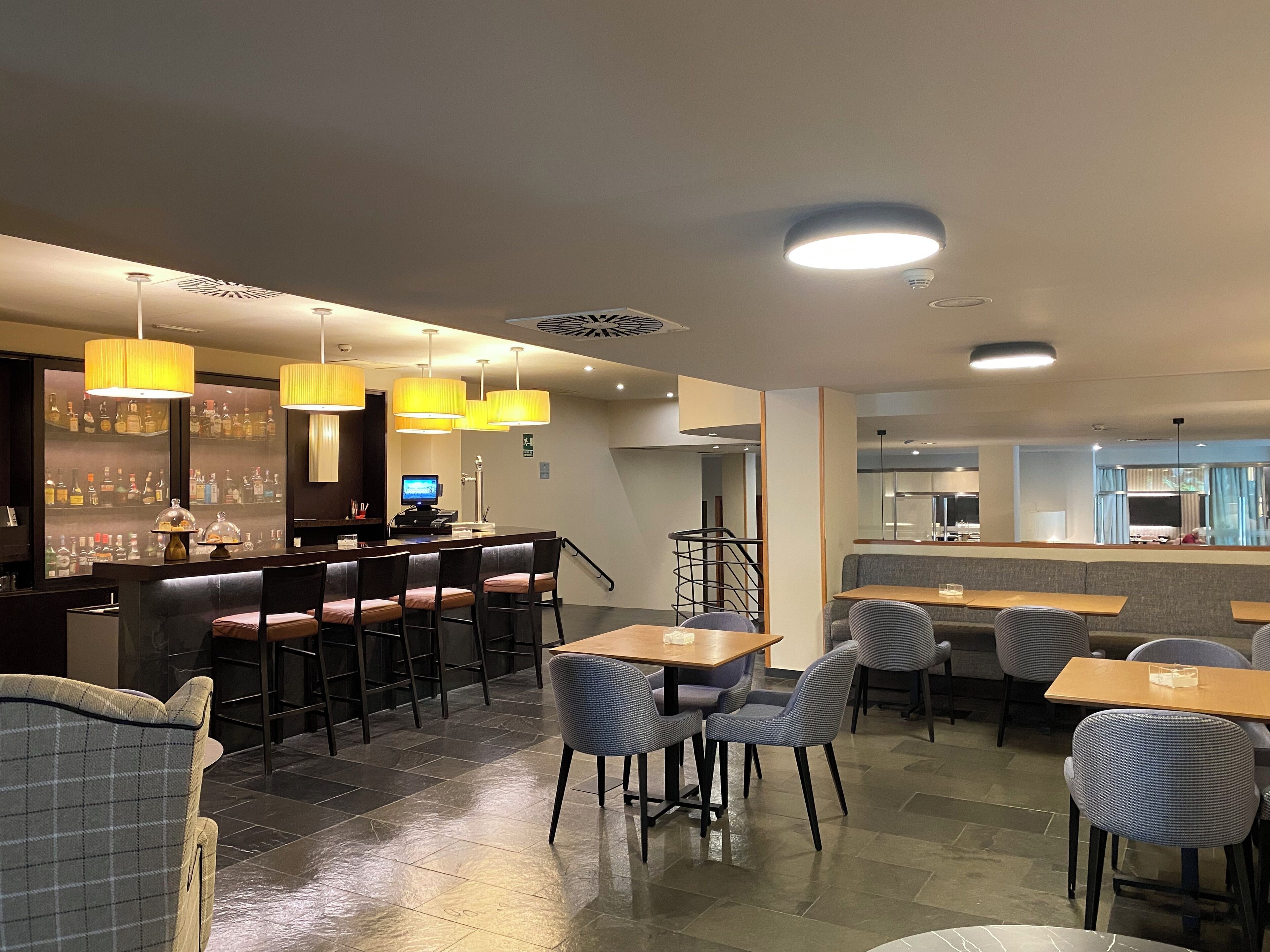 Un restaurante moderno con área de bar, diferentes disposiciones de asientos y una cocina visible al fondo.