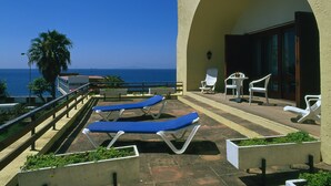 Een terras met ligbedden, een palmboom en uitzicht op zee.