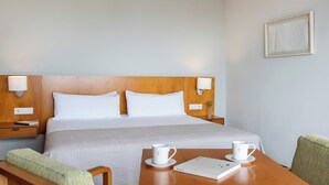 Een hotelkamer met een bed, nachtkastjes, een tafel met twee kopjes en een stoel.