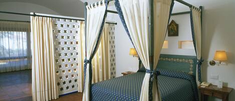 Ein Bett mit Himmelbett, ein Nachttisch mit Lampe und eine gemusterte Tagesdecke.